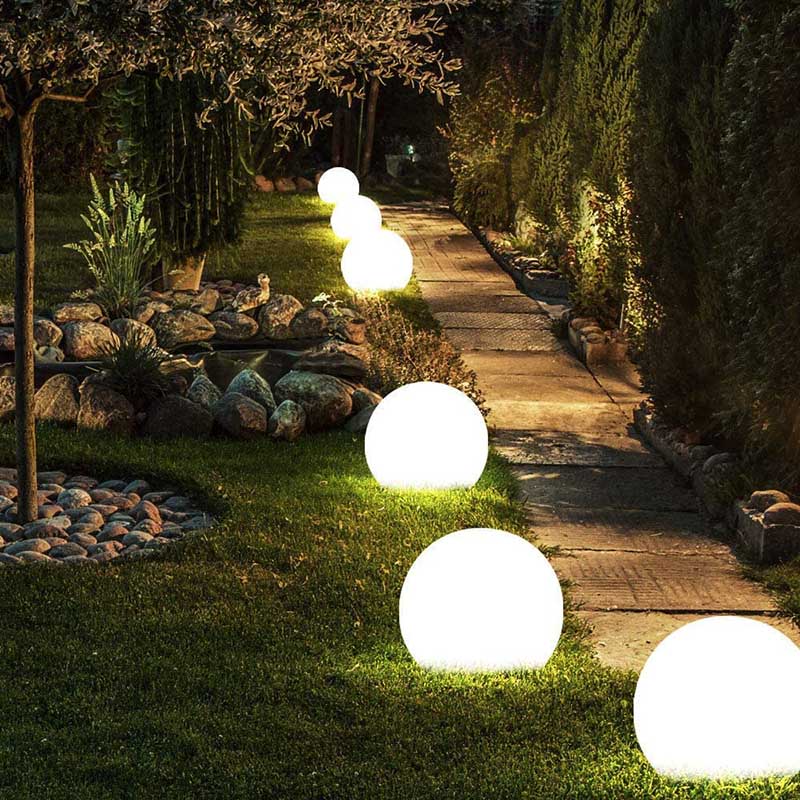 Glowing spherical garden lights on a grassy path with rocks and plants.