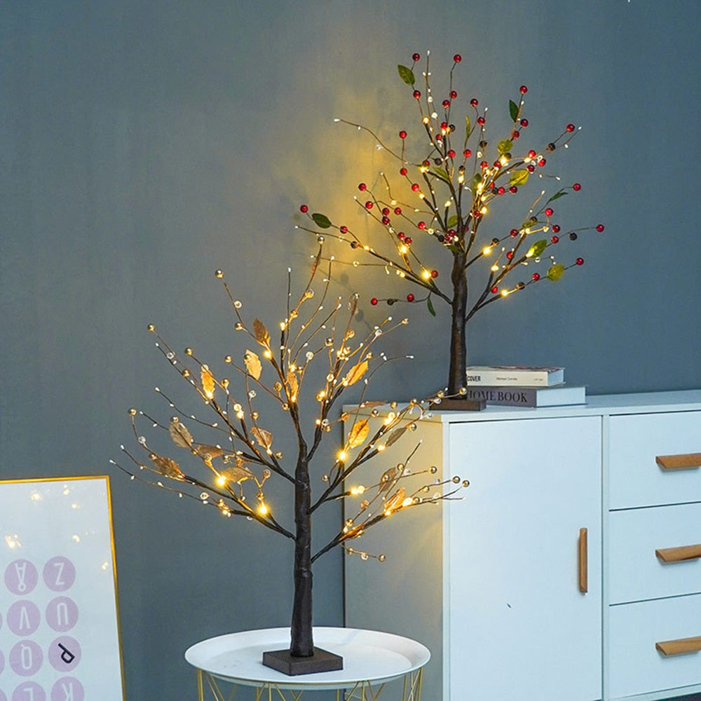 Decorative LED trees with lights on a table against a gray wall.