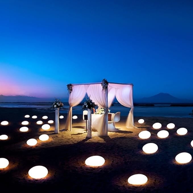 Romantic beach setting with a decorated canopy and candles on the sand at night.