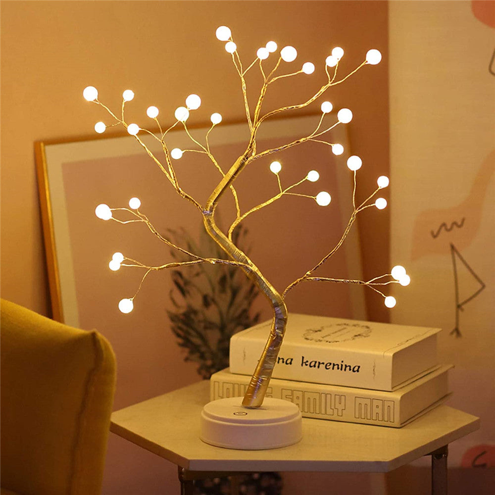 Decorative LED tree lamp on a small table with books in a cozy room setting.