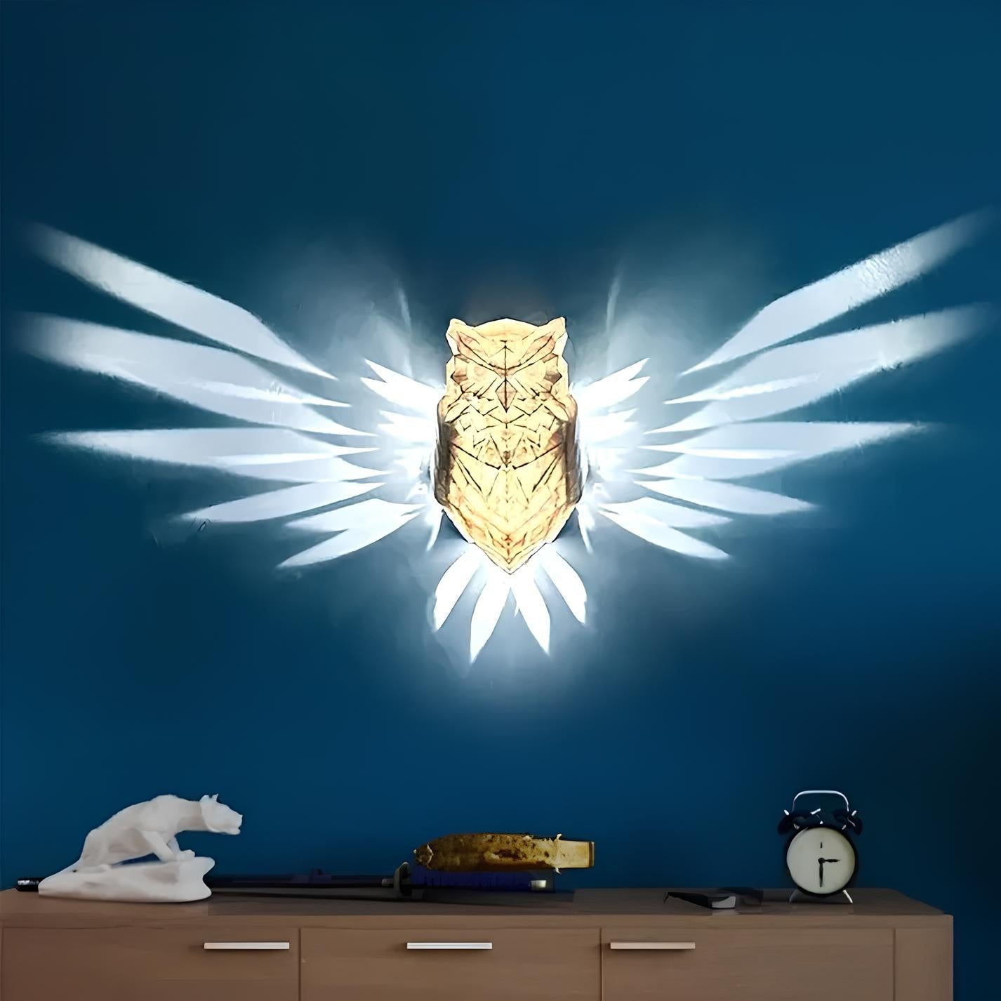 Decorative wall light shaped like an owl with wings on a blue wall above a wooden cabinet.