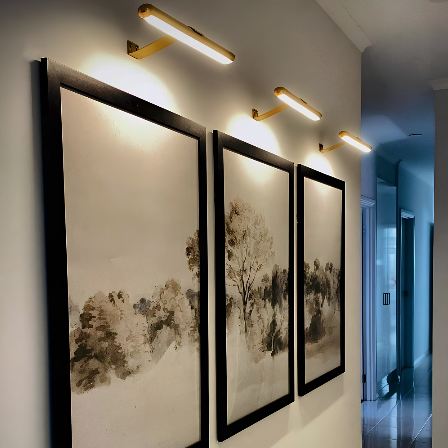 Three framed artworks on a wall with modern wall lights above