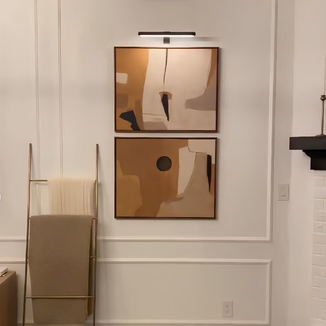 Two abstract wall art pieces on a neutral wall with a towel rack and light fixture.