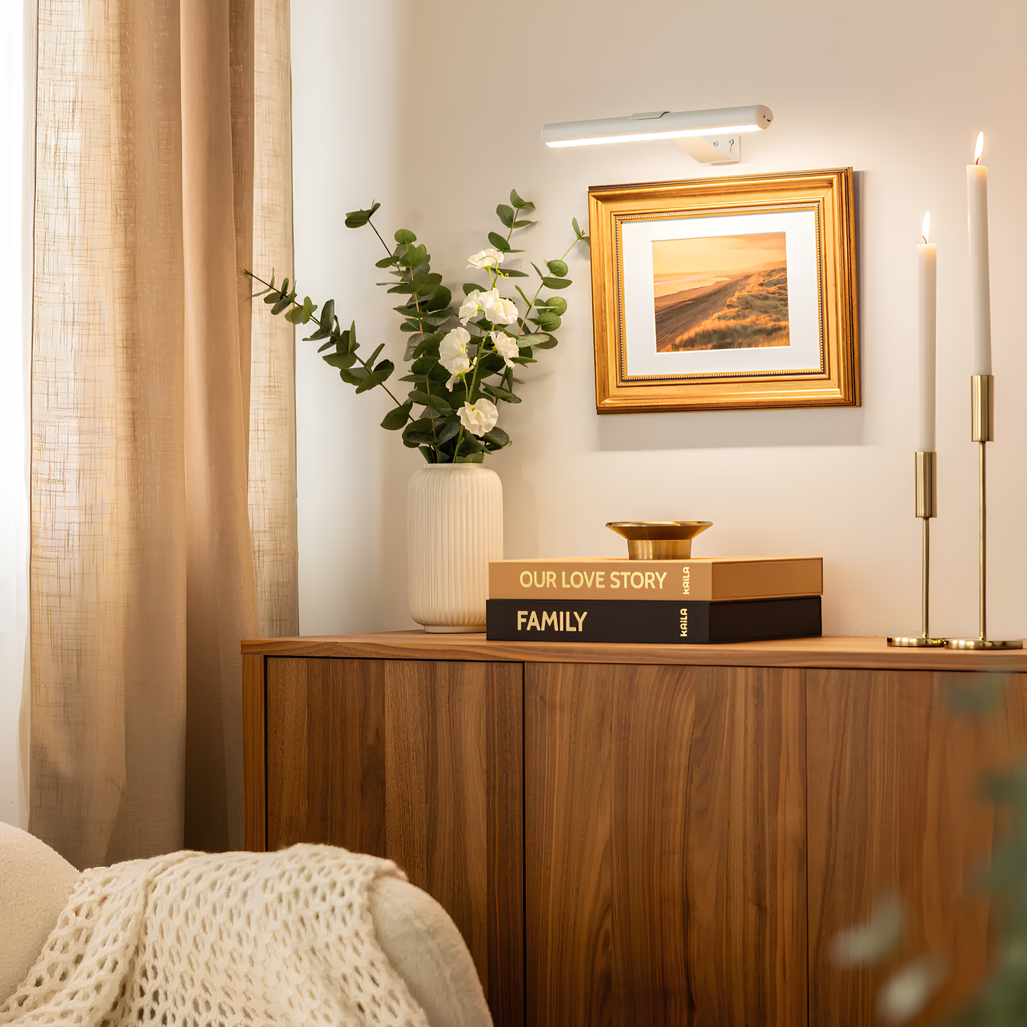 Nestled corner of a room with a wooden sideboard, books, a vase with flowers, and a framed picture.