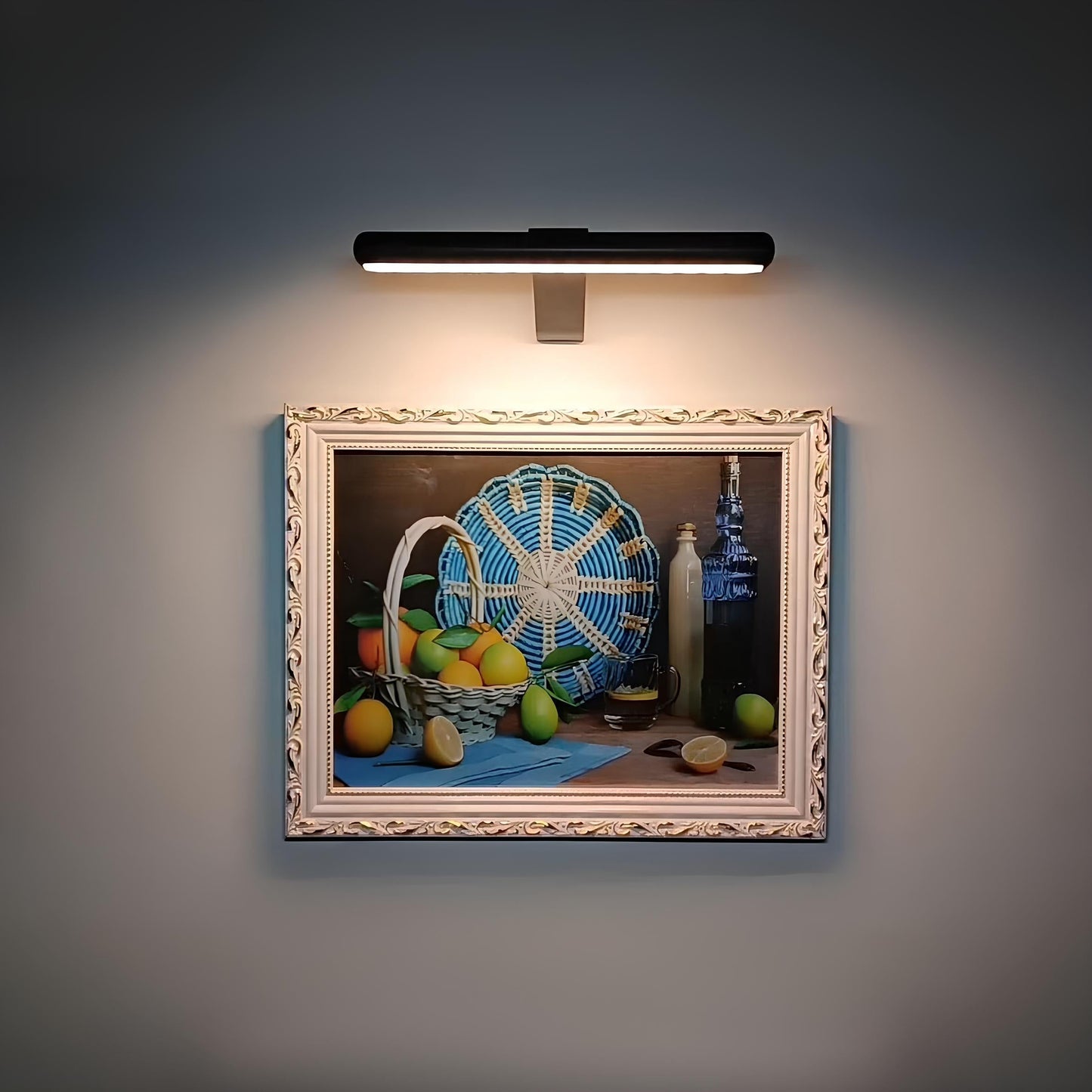 Decorative still life painting with a basket and fruits illuminated by a wall-mounted light fixture.