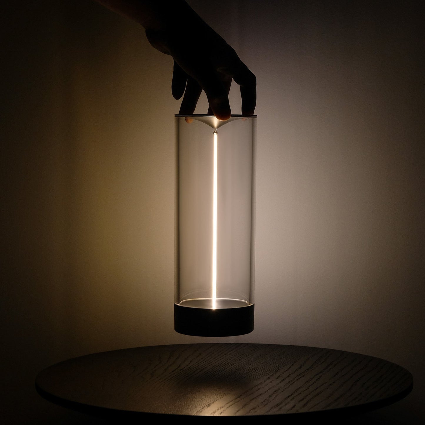 Cylindrical glass light with black base held by a hand against a dark background