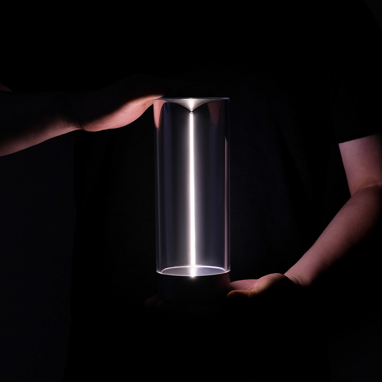 Cylindrical light held by hands against a dark background