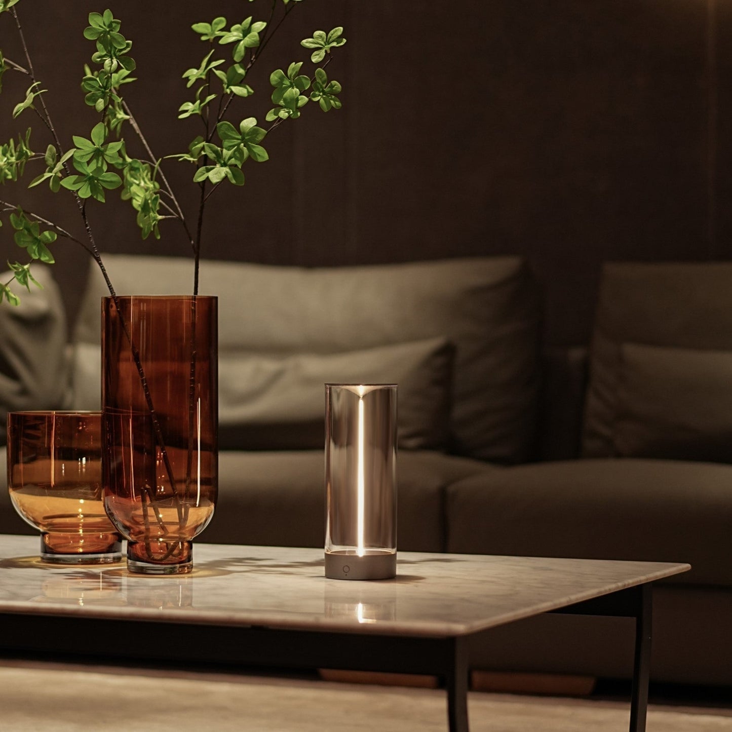 Decorative glass vases with greenery on a coffee table in a living room setting.