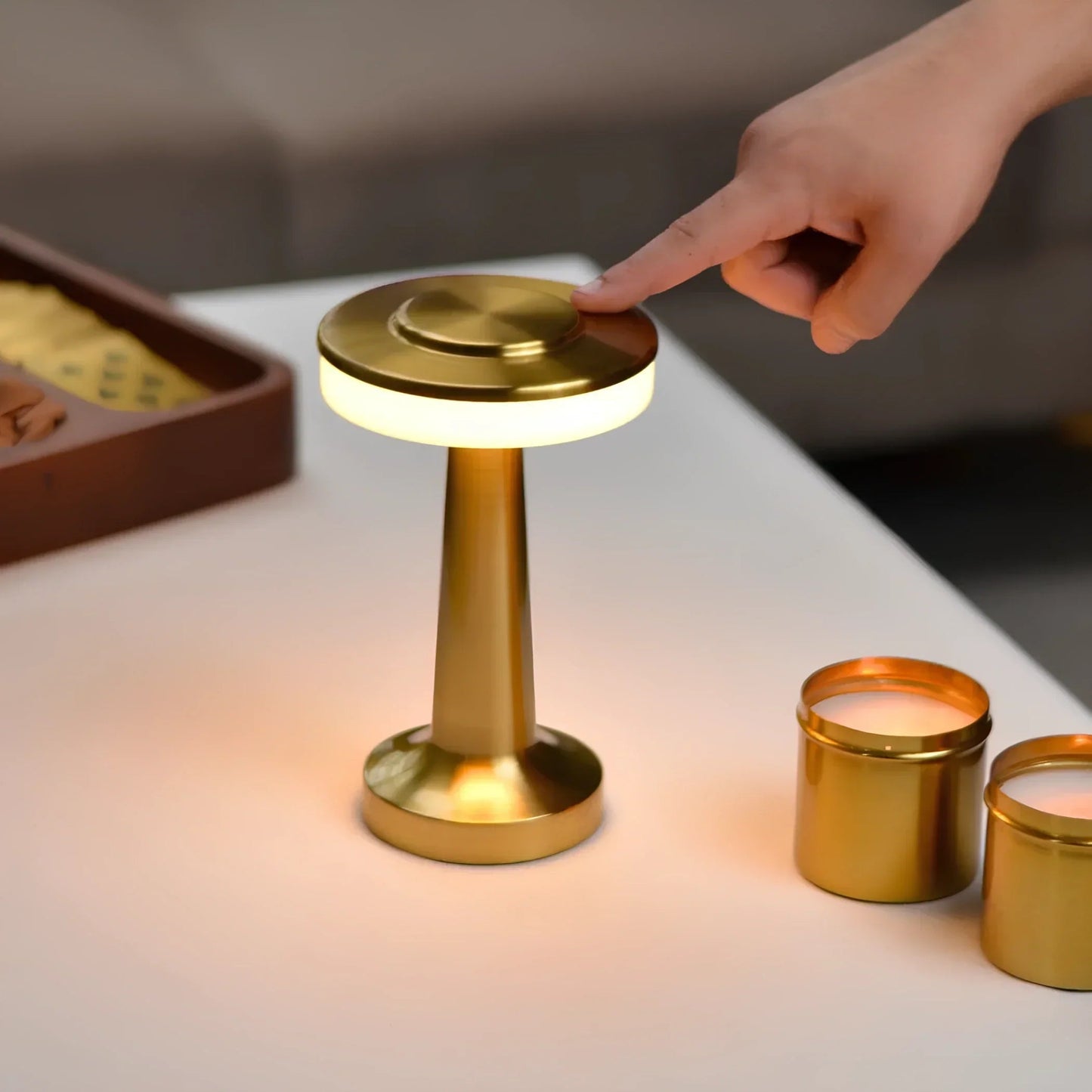 Gold lamp being turned on with a hand, surrounded by candles on a table.