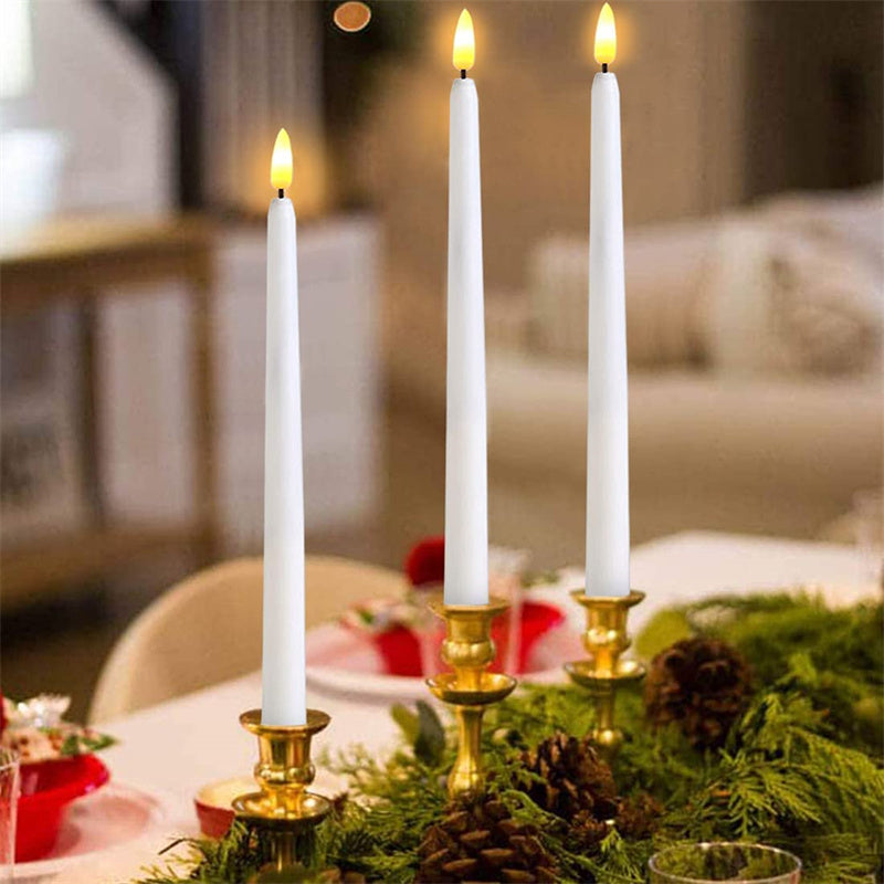 Three white candles in gold candle holders on a table with greenery and red decorations.