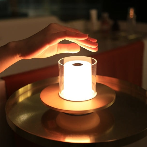 Hand reaching towards a glowing cylindrical light on a reflective surface with a blurred background