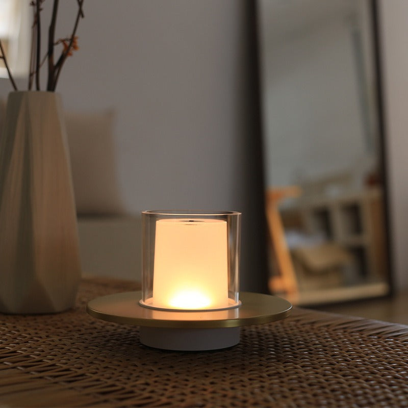 Small lit candle in a glass holder on a woven surface with a blurred indoor background
