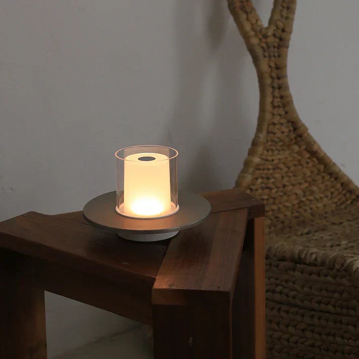 Candle in a glass holder on a wooden surface with a wicker chair in the background