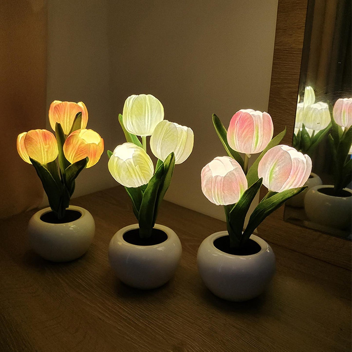 Three potted tulip-shaped lamps on a wooden surface with a mirror reflecting the scene.