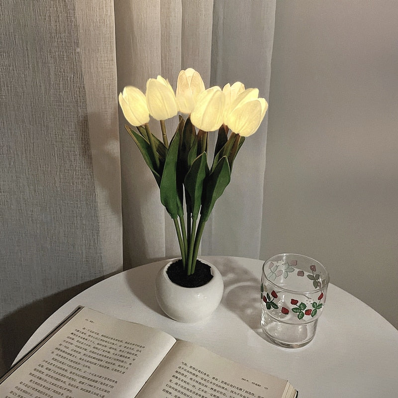 Potted plant with glowing bulbs on a table next to an open book and a glass.