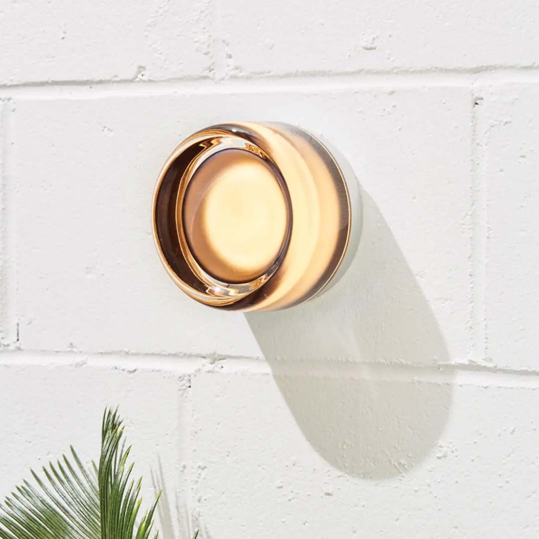 Wall-mounted outdoor light fixture on a white brick wall with a plant in the foreground.