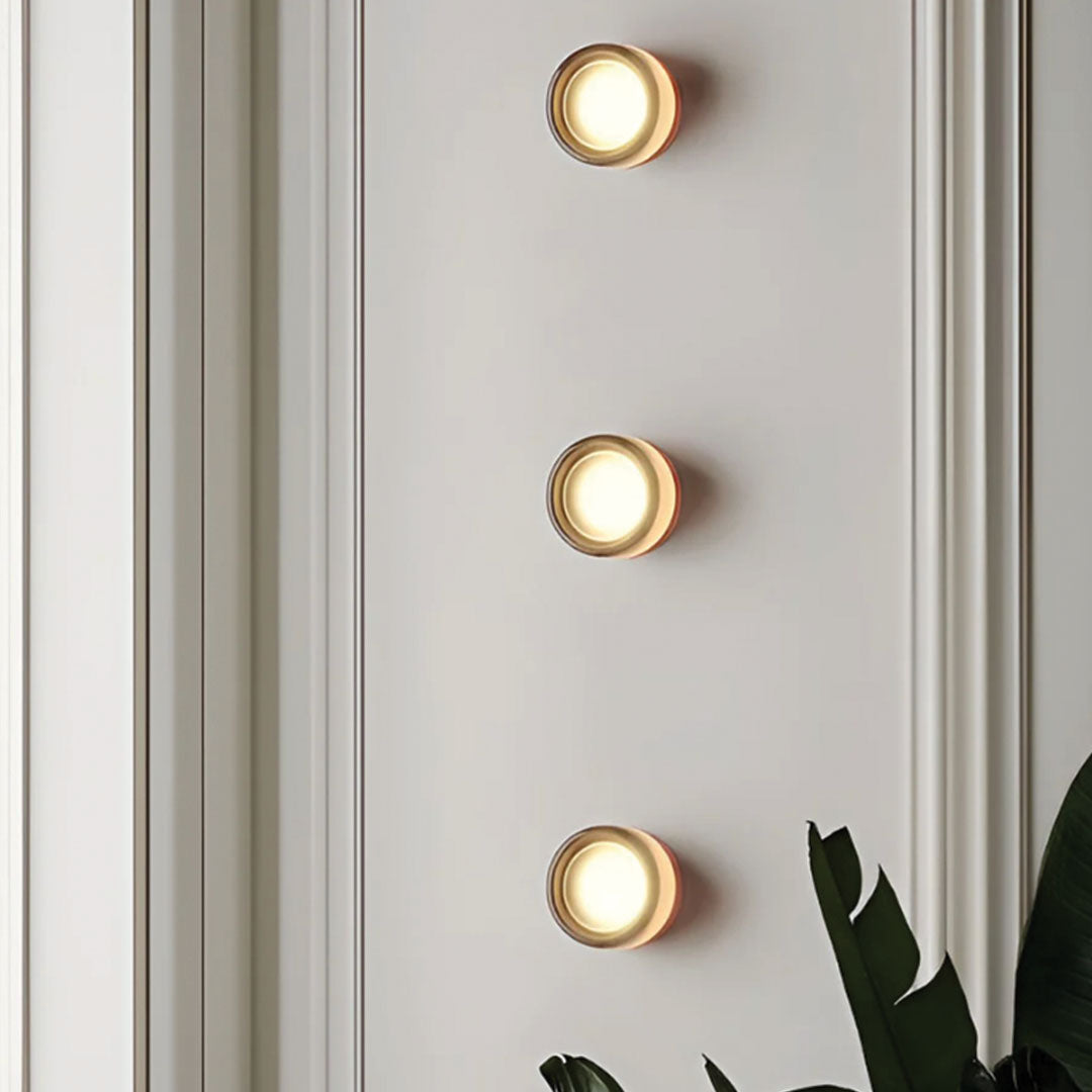 Three round wall lights on a light gray wall with a plant in the corner.