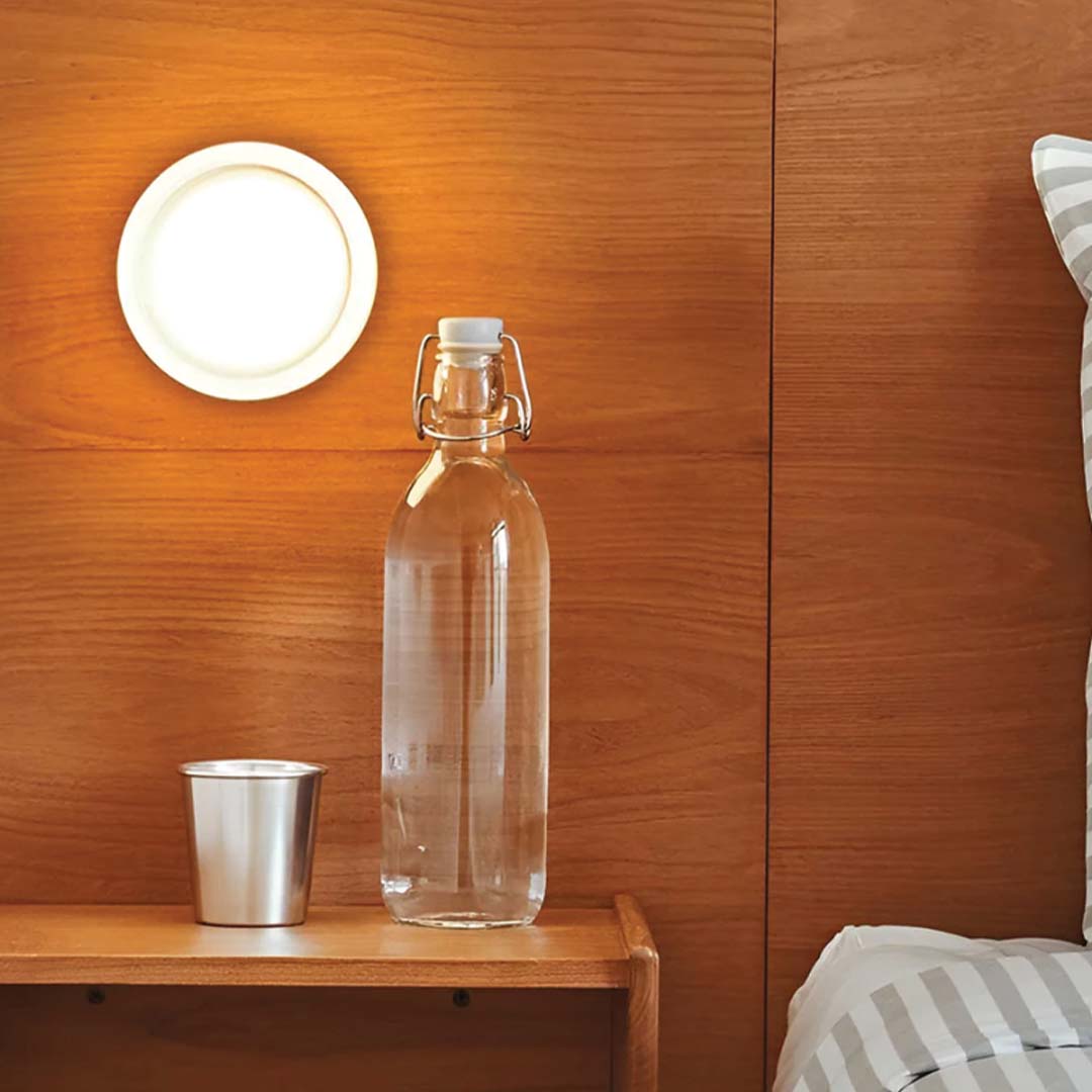 Clear glass bottle and silver cup on a wooden surface with a wooden wall and striped fabric in the background.