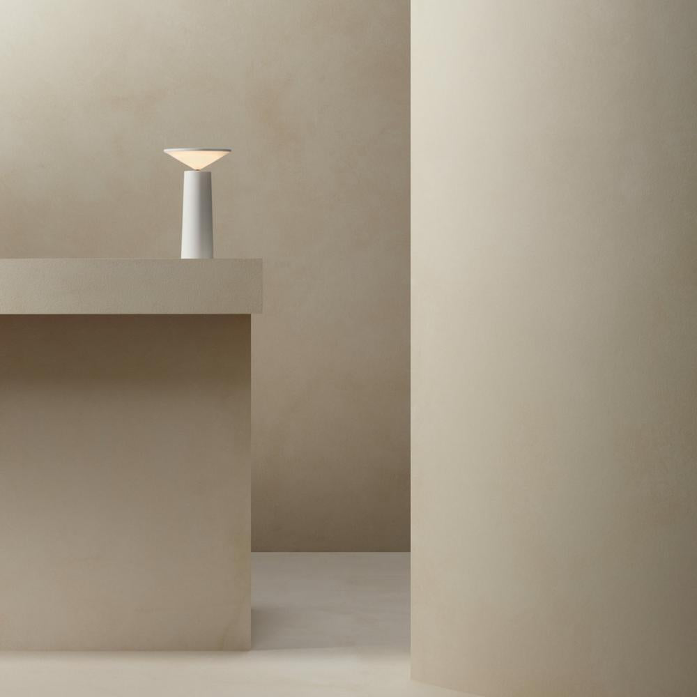 Minimalist scene with a lamp on a concrete surface against a plain wall.