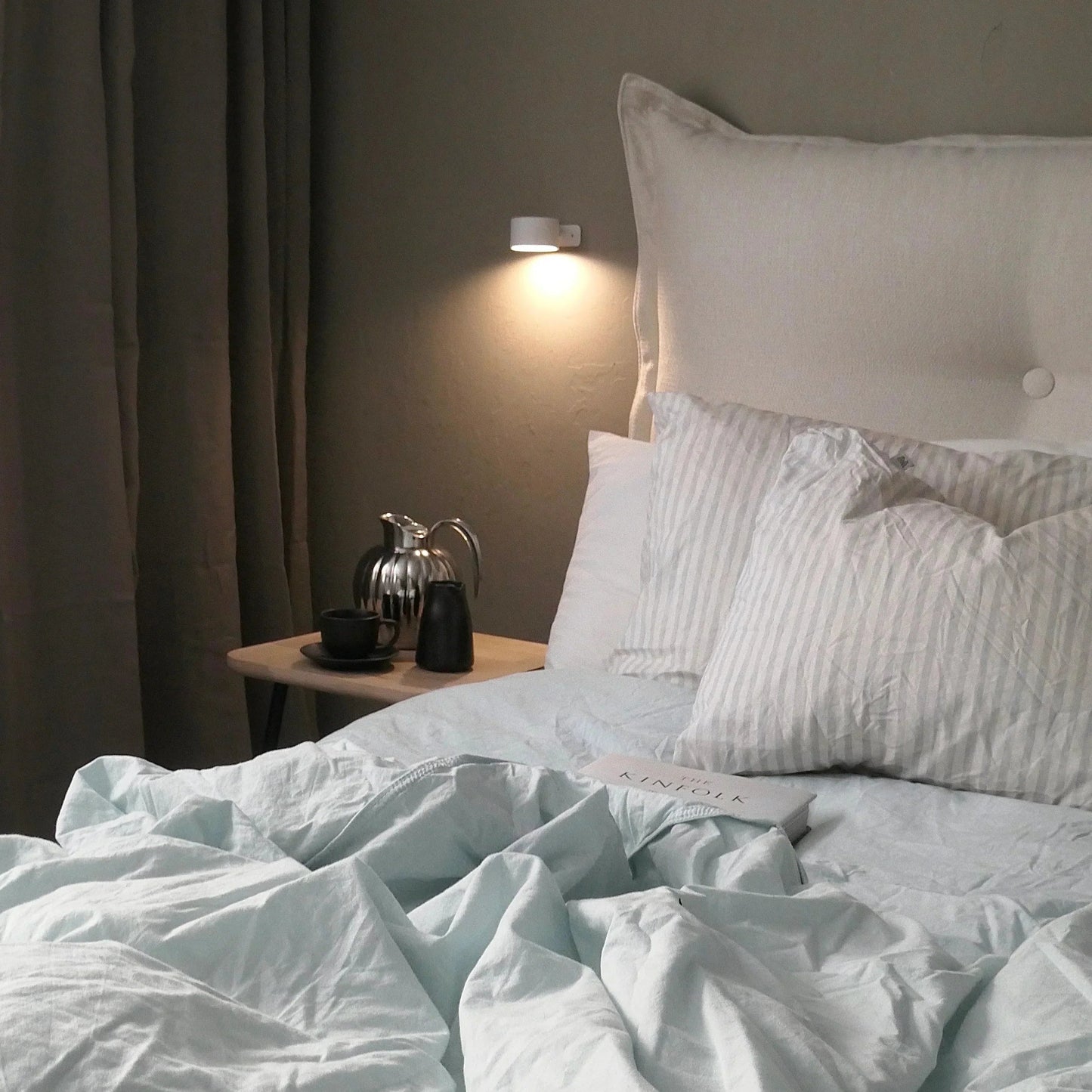 Neatly made bed with light blue bedding and white pillows in a dimly lit bedroom.