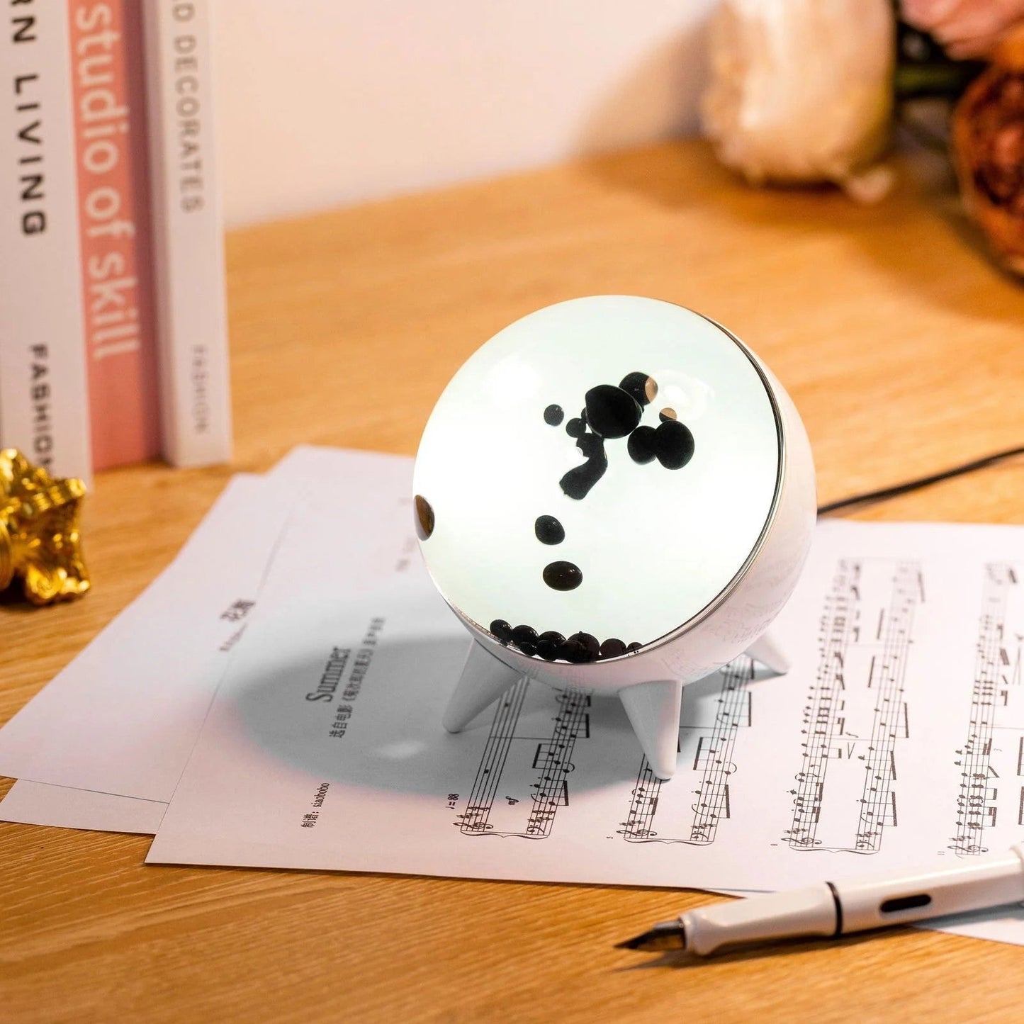 Round white object with black dots on a wooden surface with books and a pen.