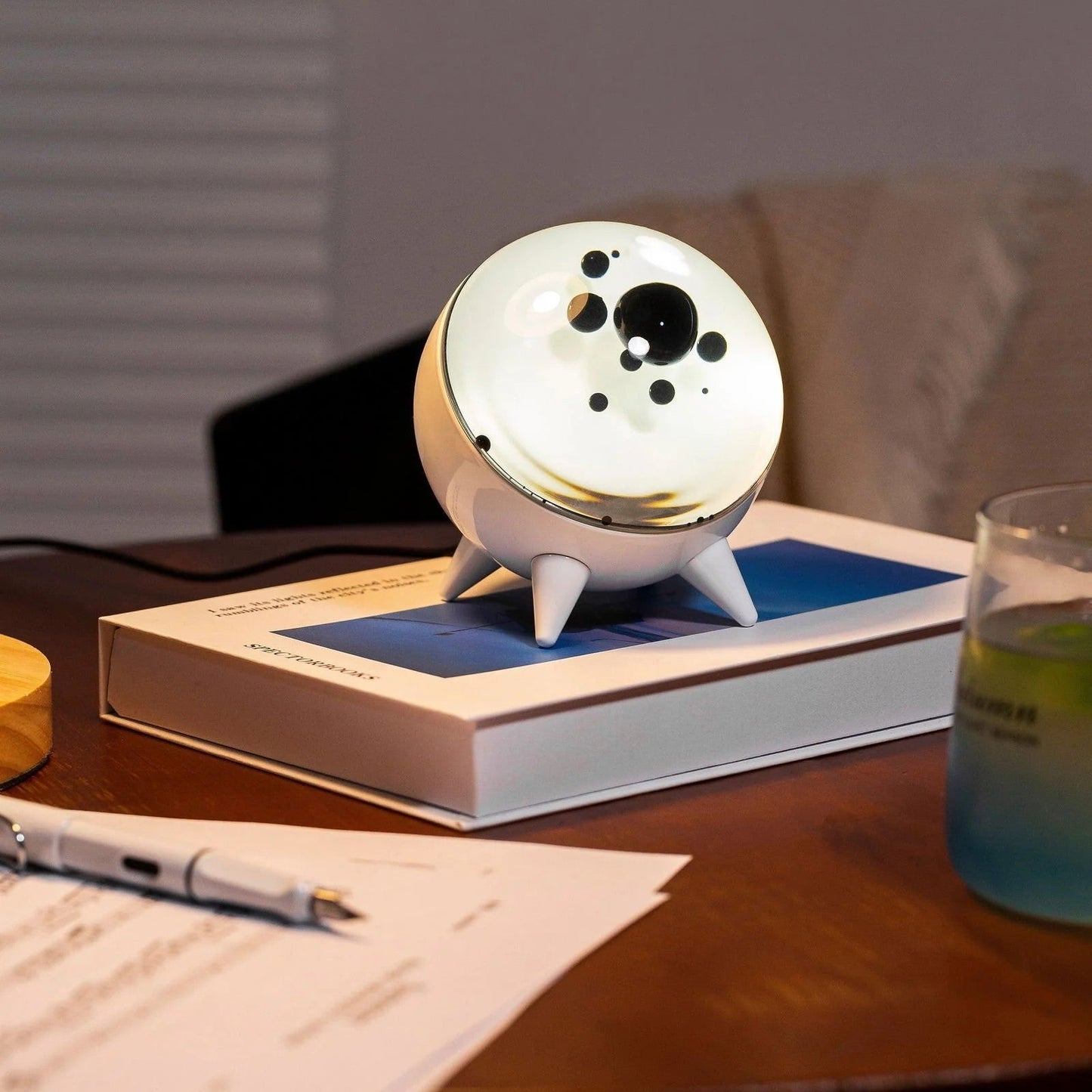 White spherical robot on a book with a pen and glass in the foreground