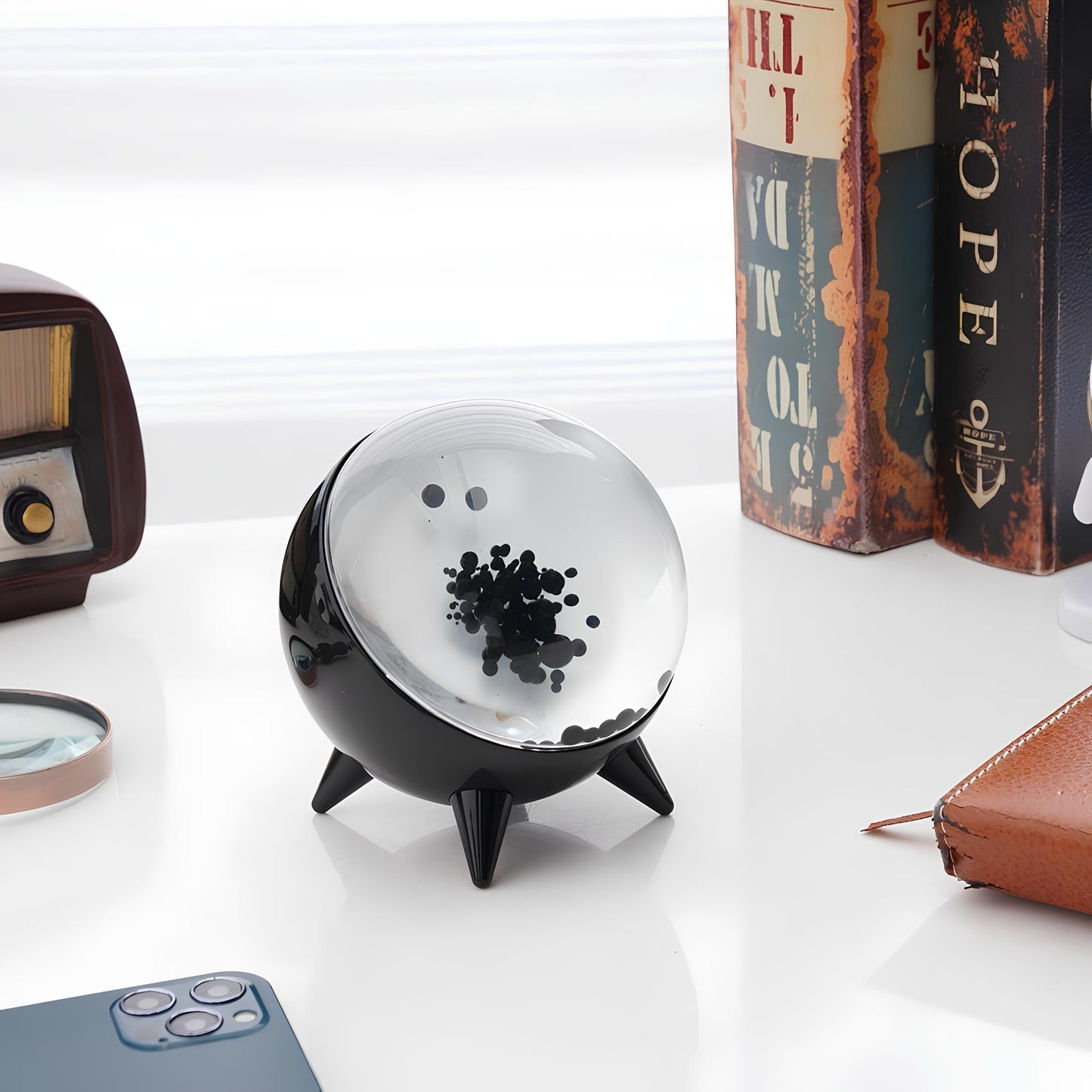Decorative black and clear sphere on a white surface with books and a magnifying glass in the background.