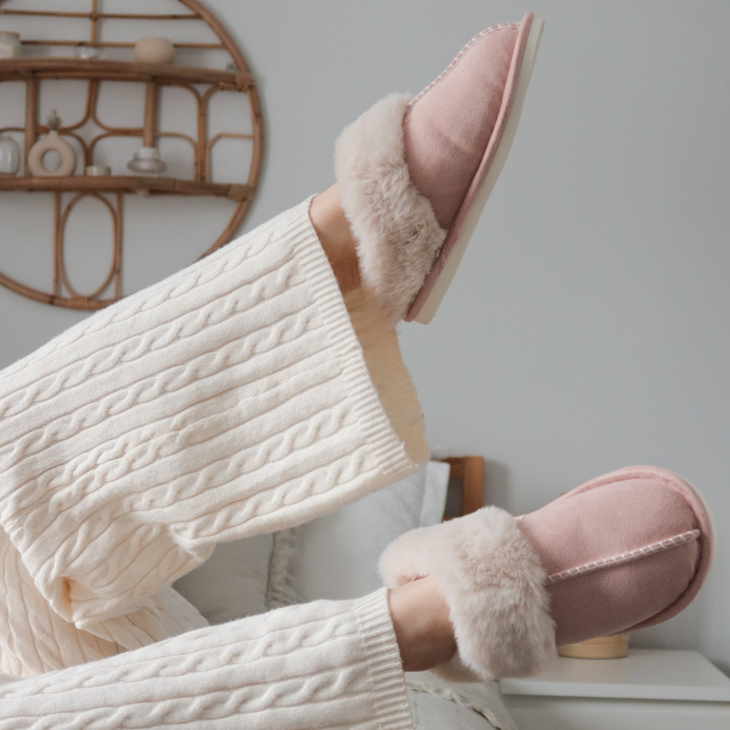 Person wearing pink slippers with fluffy interior, sitting on a chair.