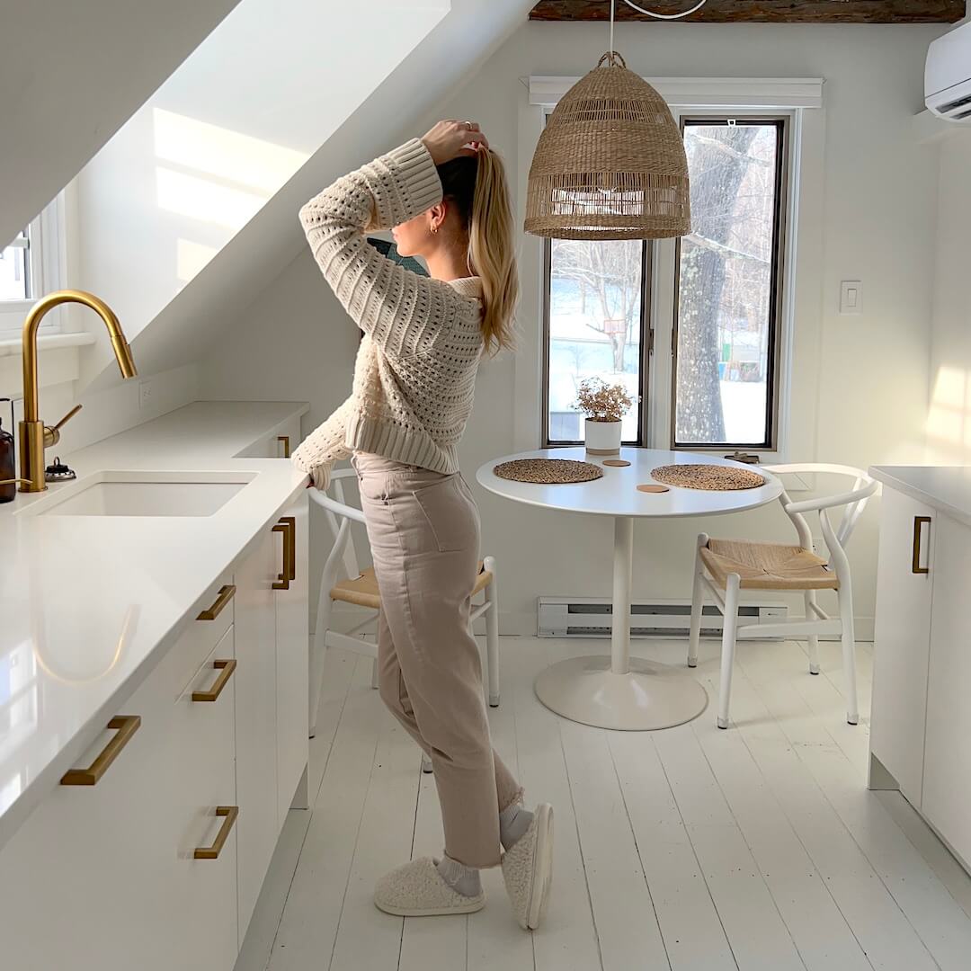 Person standing in a modern kitchen with white cabinets and gold fixtures.