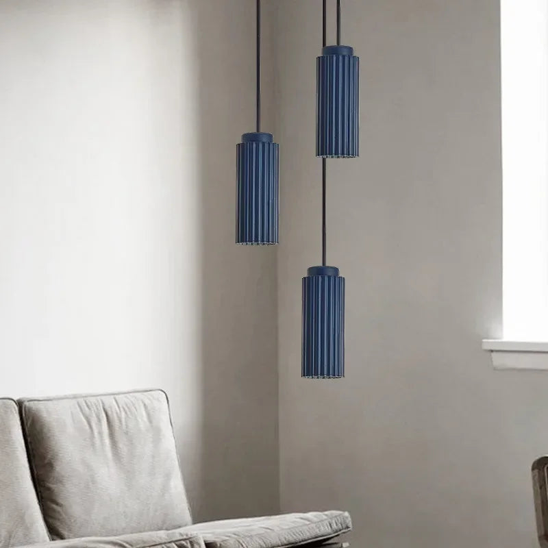 Three blue cylindrical pendant lights hanging above a gray sofa against a light gray wall.