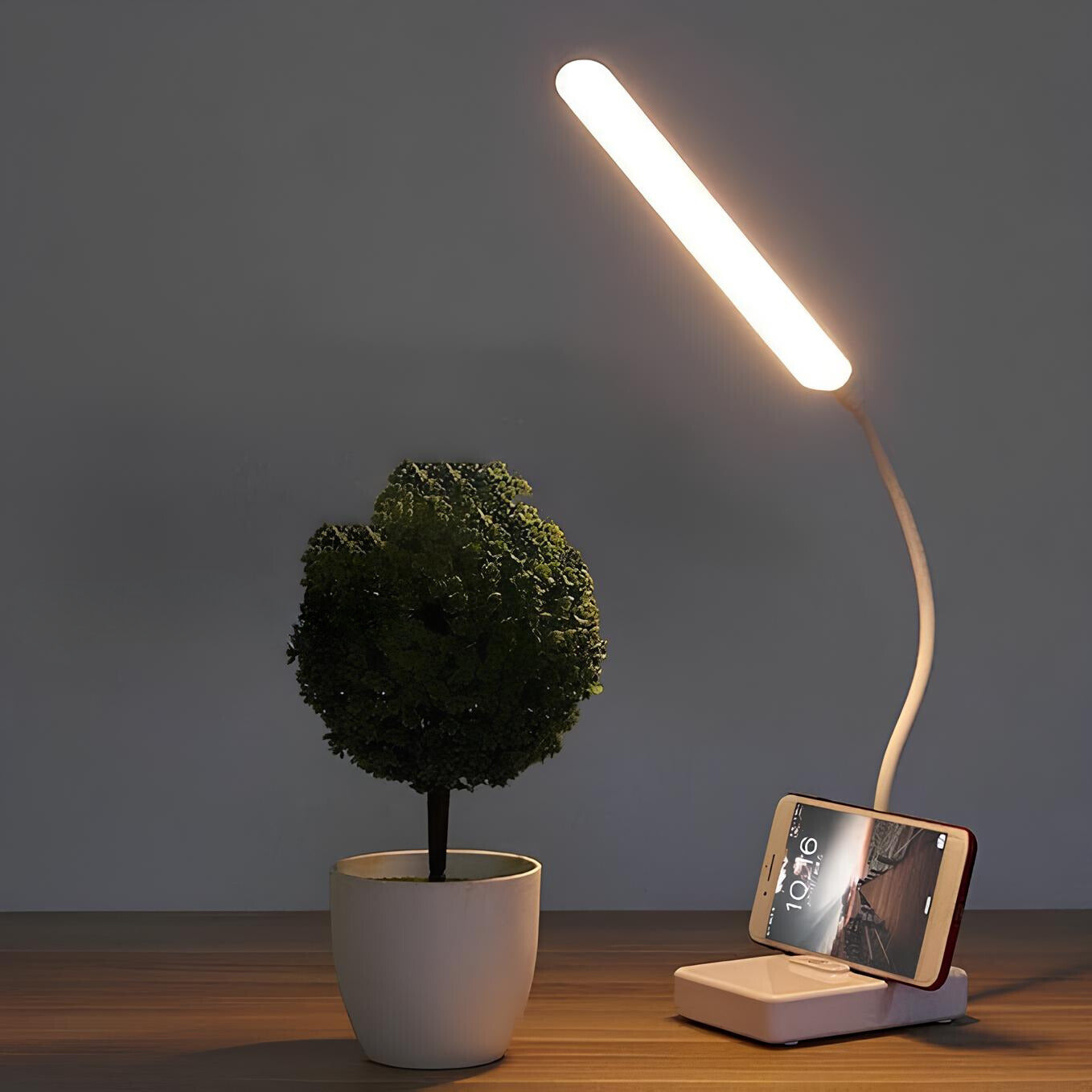 Table lamp with phone charging stand next to a potted plant on a wooden surface.