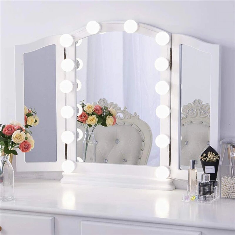 Tri-fold vanity mirror with lights on a white dresser with decorative items.