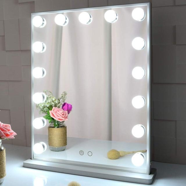 Makeup mirror with lights on a white surface with flowers and a brush.
