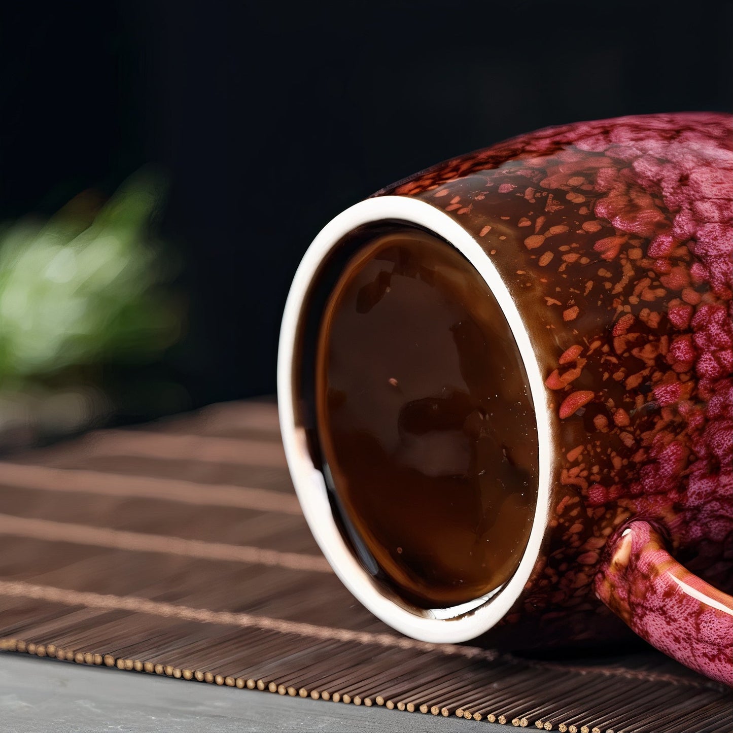 Red ceramic cup with a floral pattern filled with dark liquid on a wooden surface.