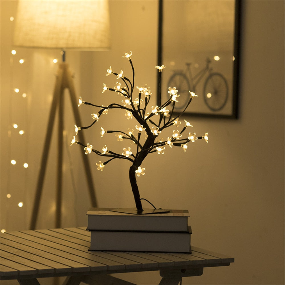 Decorative LED tree on books with warm glow in a softly lit room.