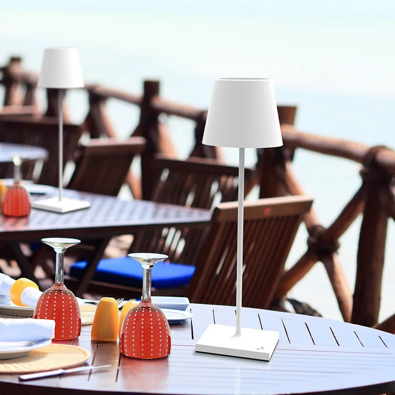 White floor lamp on a table with outdoor furniture and water in the background