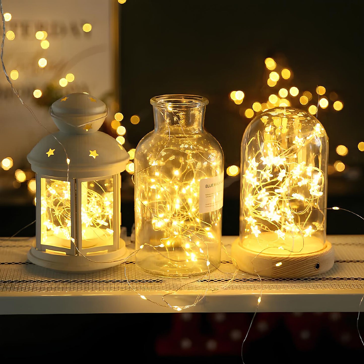 Decorative lanterns and jars with string lights on a table with a blurred background of lights.