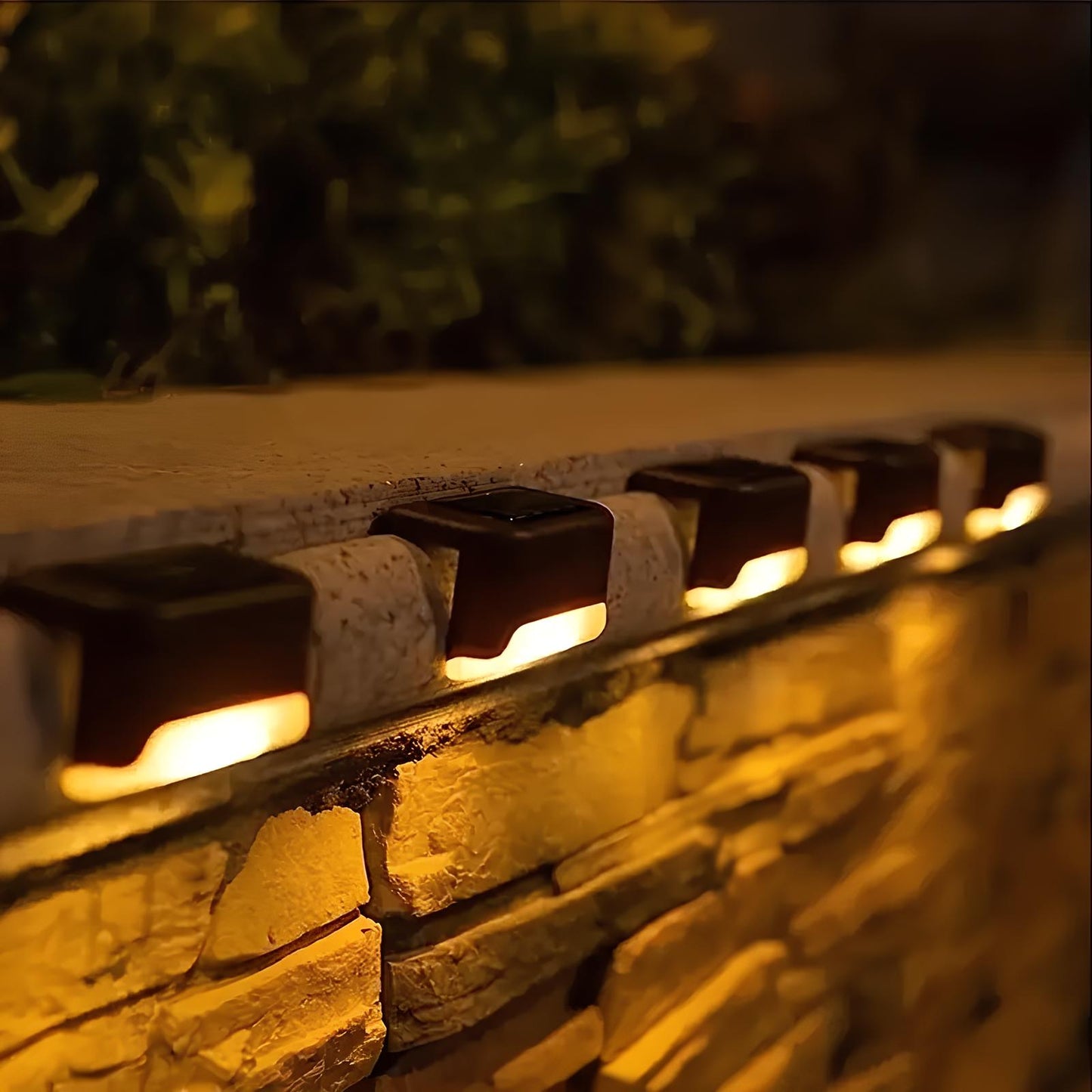 Row of solar-powered outdoor lights on a stone wall with a blurred greenery background