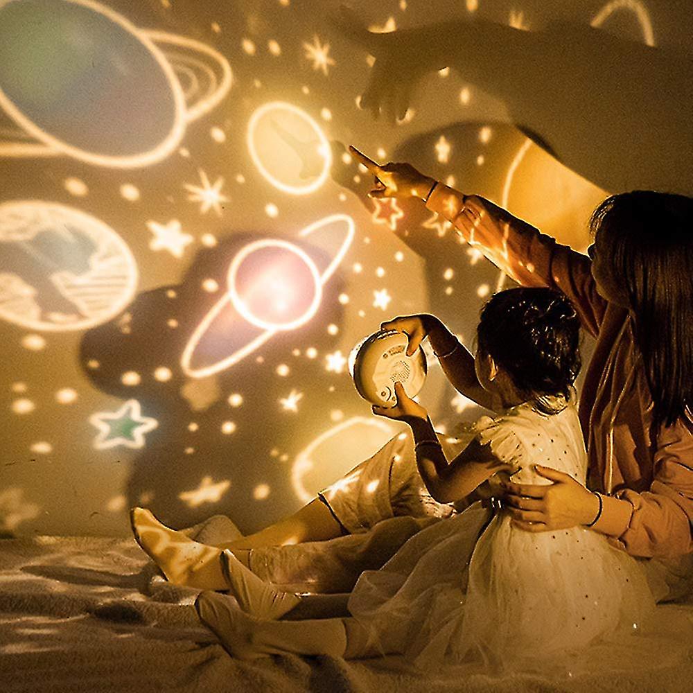 Two children pointing at a starry night sky projection on a wall.