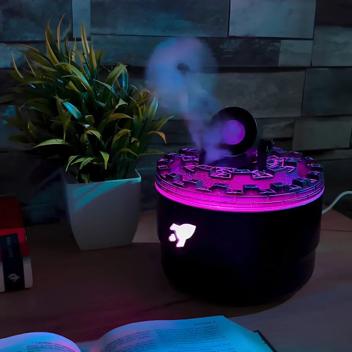Black diffuser with purple light on a table next to a plant and open book
