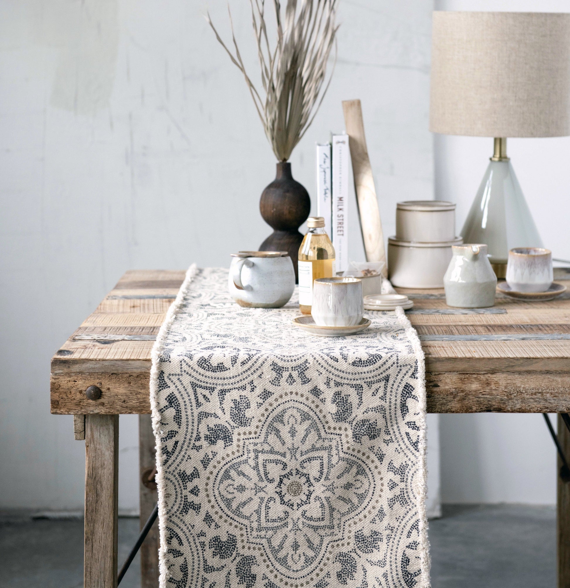 Decorative table setting with a patterned table runner on a wooden table.