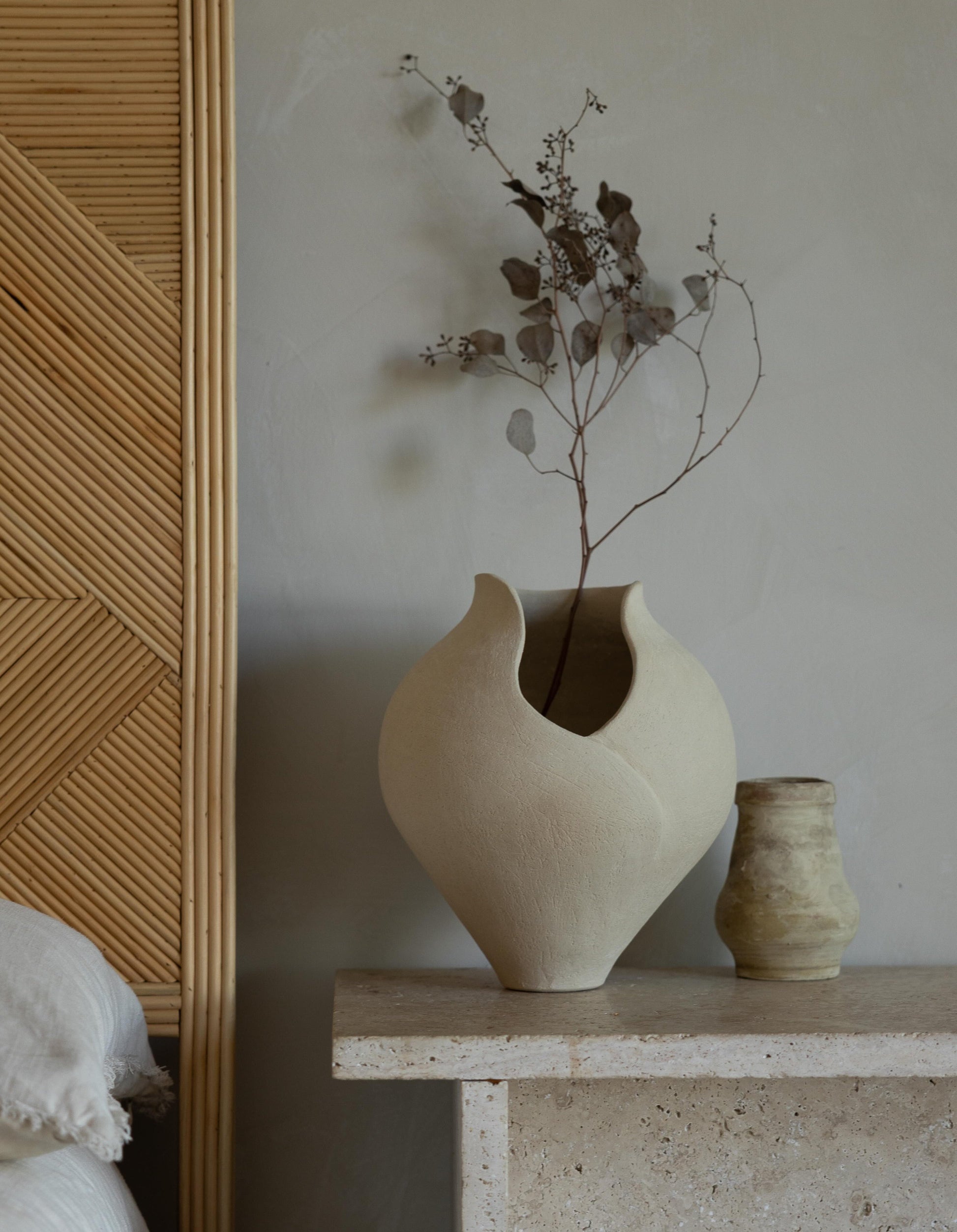 Ceramic vase with dried plant on a stone surface against a neutral wall.