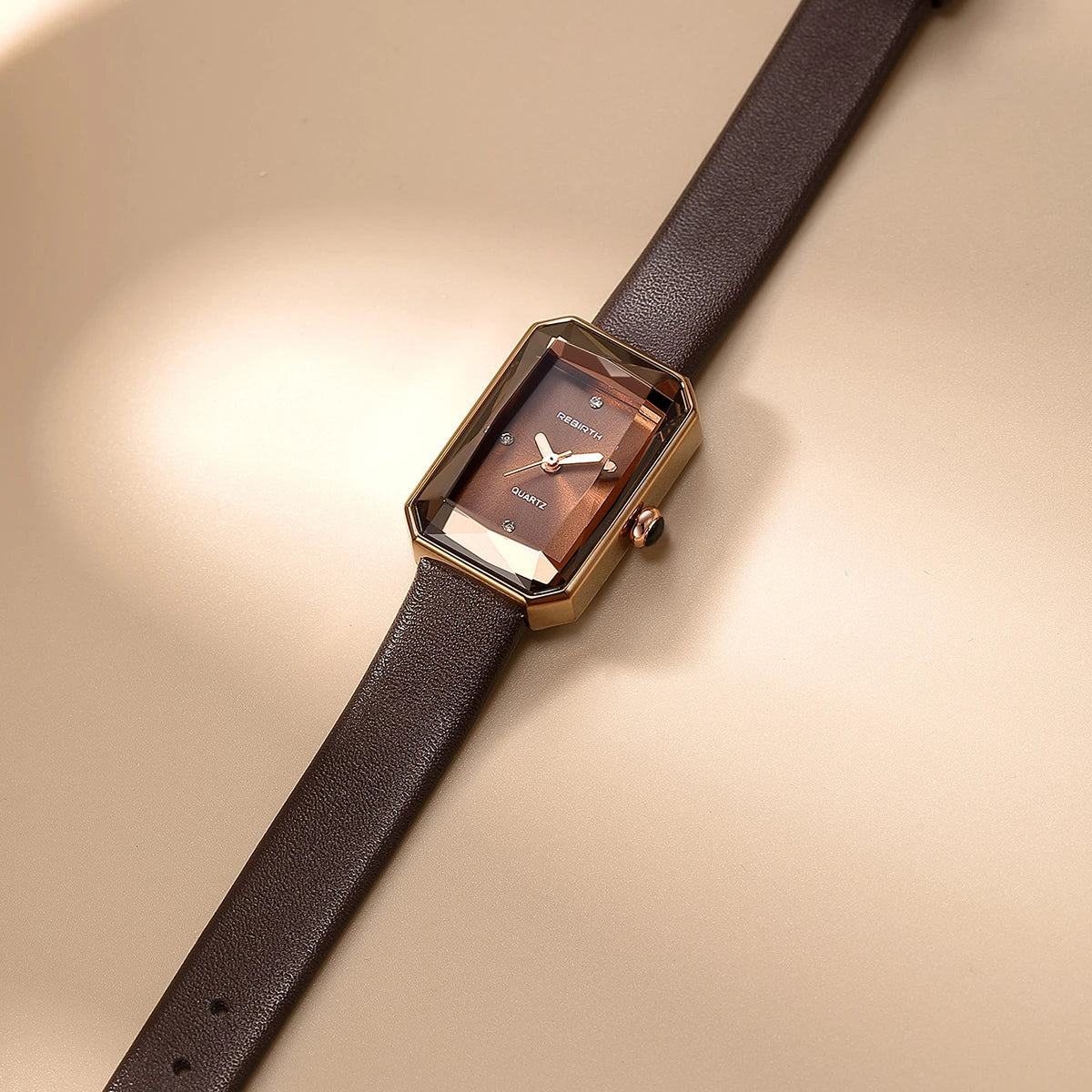Rectangular watch with brown strap and rose gold case on beige background