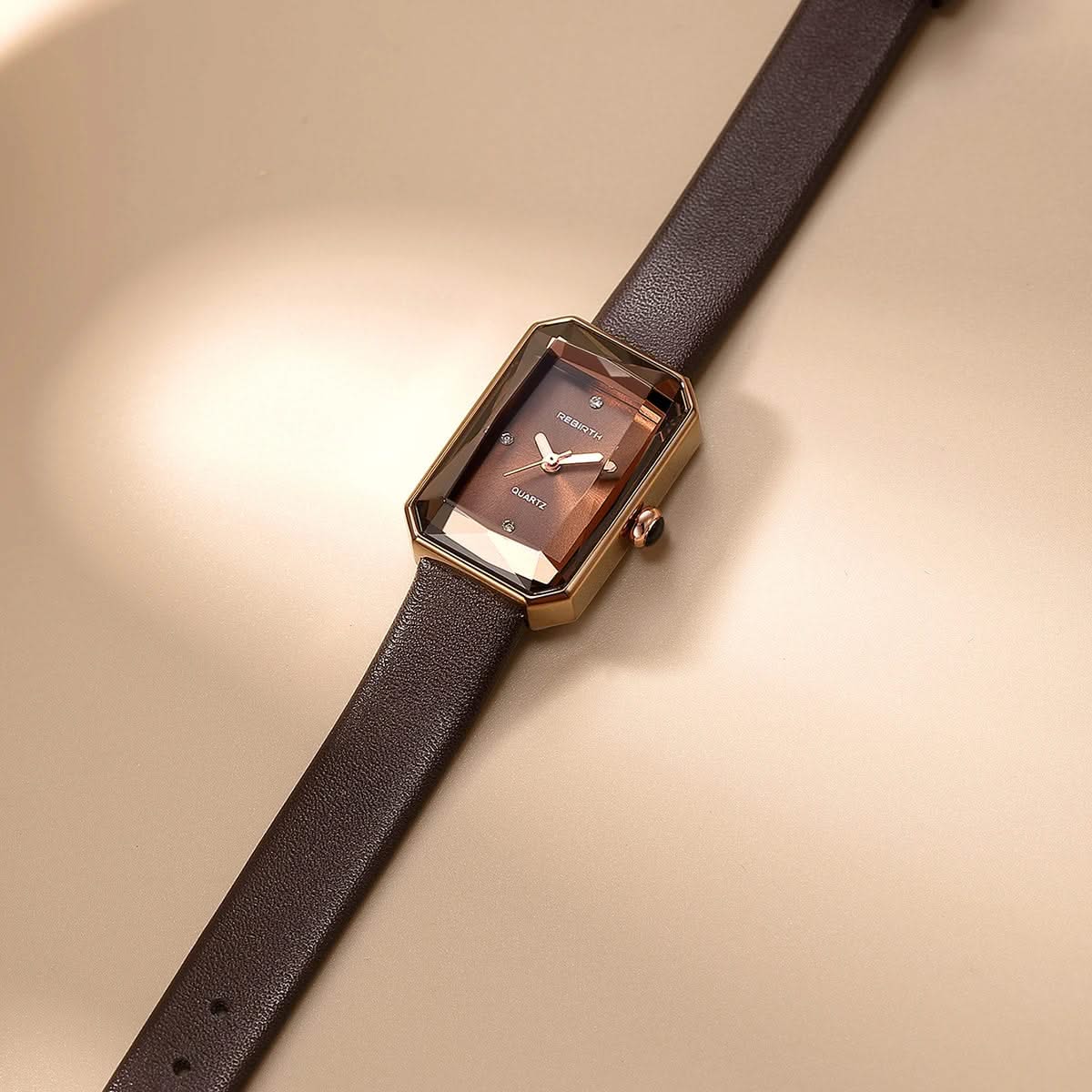 Rectangular watch with brown strap and rose gold case on beige background
