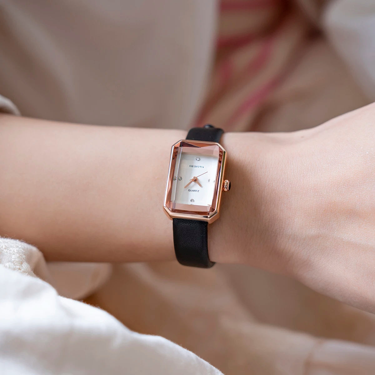 Wrist wearing a black watch with a rose gold case on a blurred background