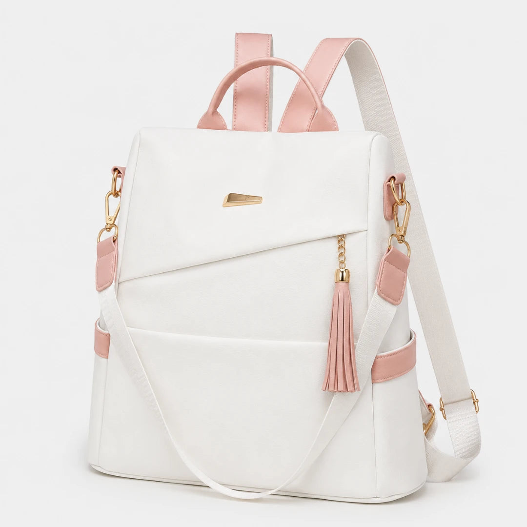 Josh & Tate - AntiTheft™ Oxford Backpack - A white backpack with light pink leather-like accents, gold-tone hardware, and a pink tassel charm, shown on a clean white background.