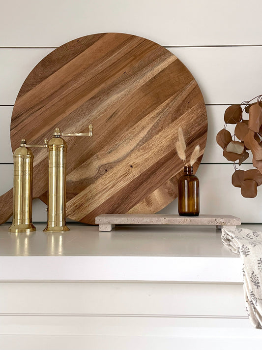 Wooden cutting board on a shelf with decorative items against a white wall.