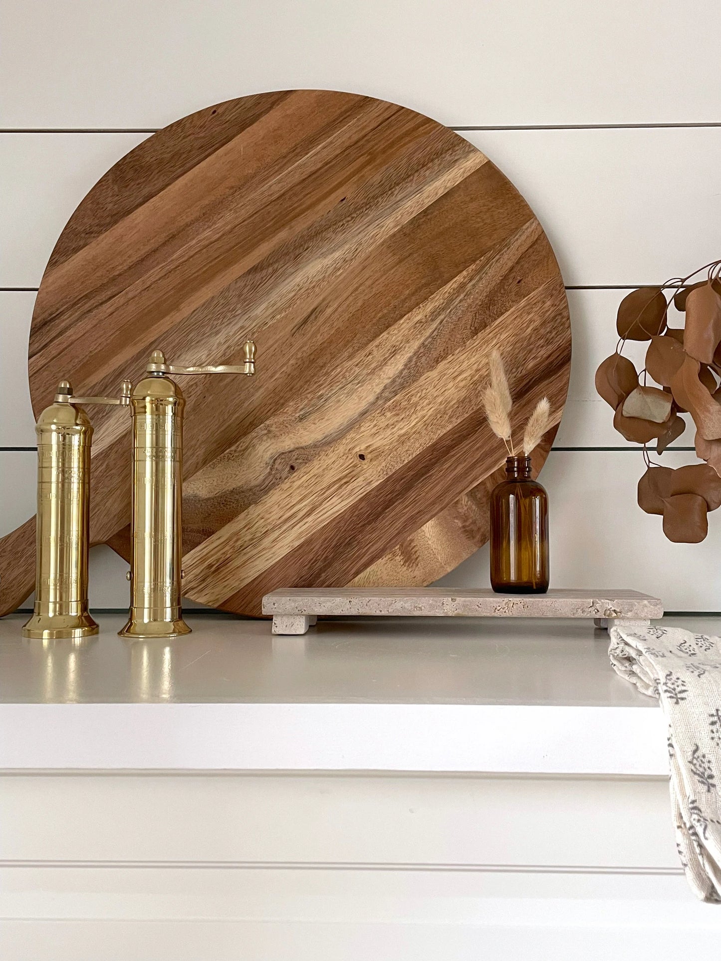 Josh & Tate - Arbor Round Wooden Board - Wooden cutting board with brass faucets and bottles on a white surface