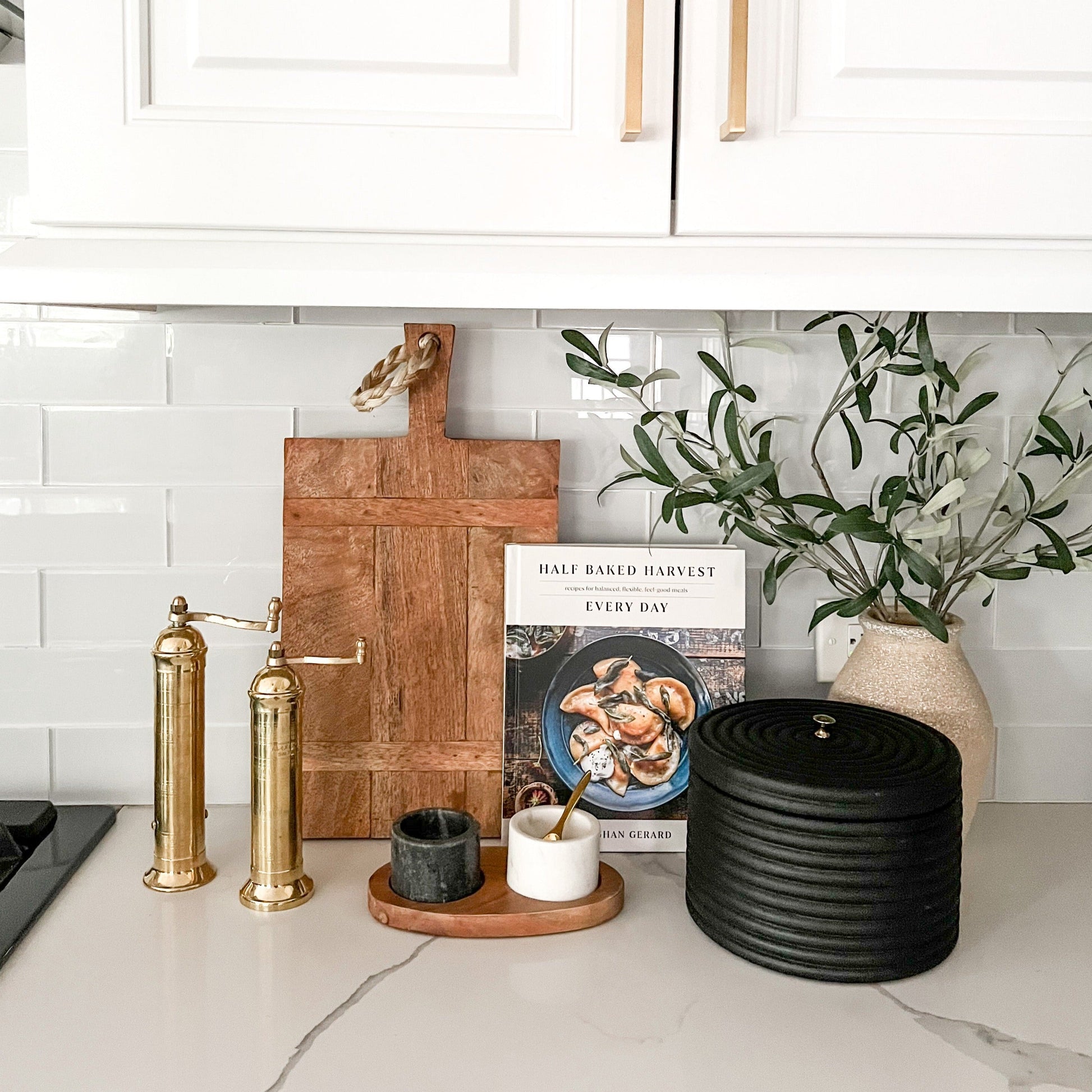 Kitchen counter with cutting board, cookbooks, and decorative items against a white tiled wall.