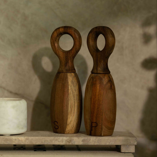 Two wooden salt and pepper shakers on a stone surface with a neutral background